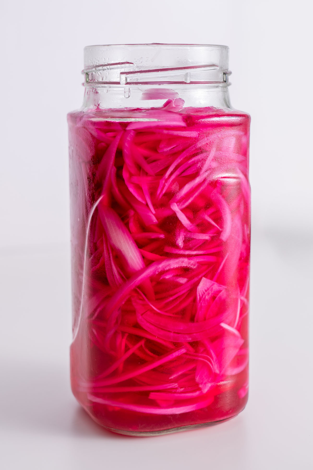 Close-up of bright pink pickled red onions in a glass jar.