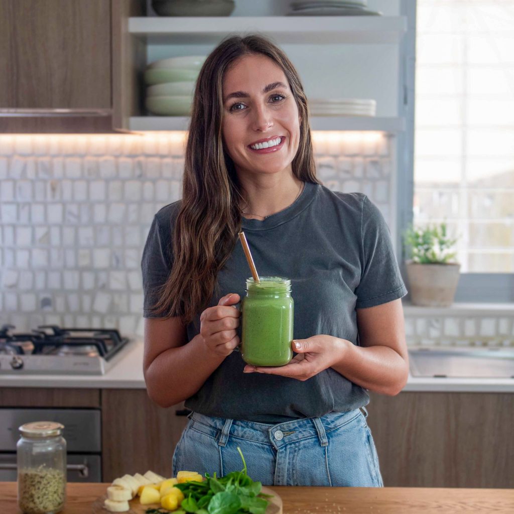 Sarah Cobacho standing in the plantbaes kitchen with a green smoothie