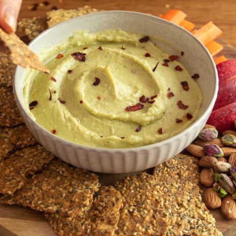 A bowl of creamy avocado bean dip surrounded by homemade nourishing crackers