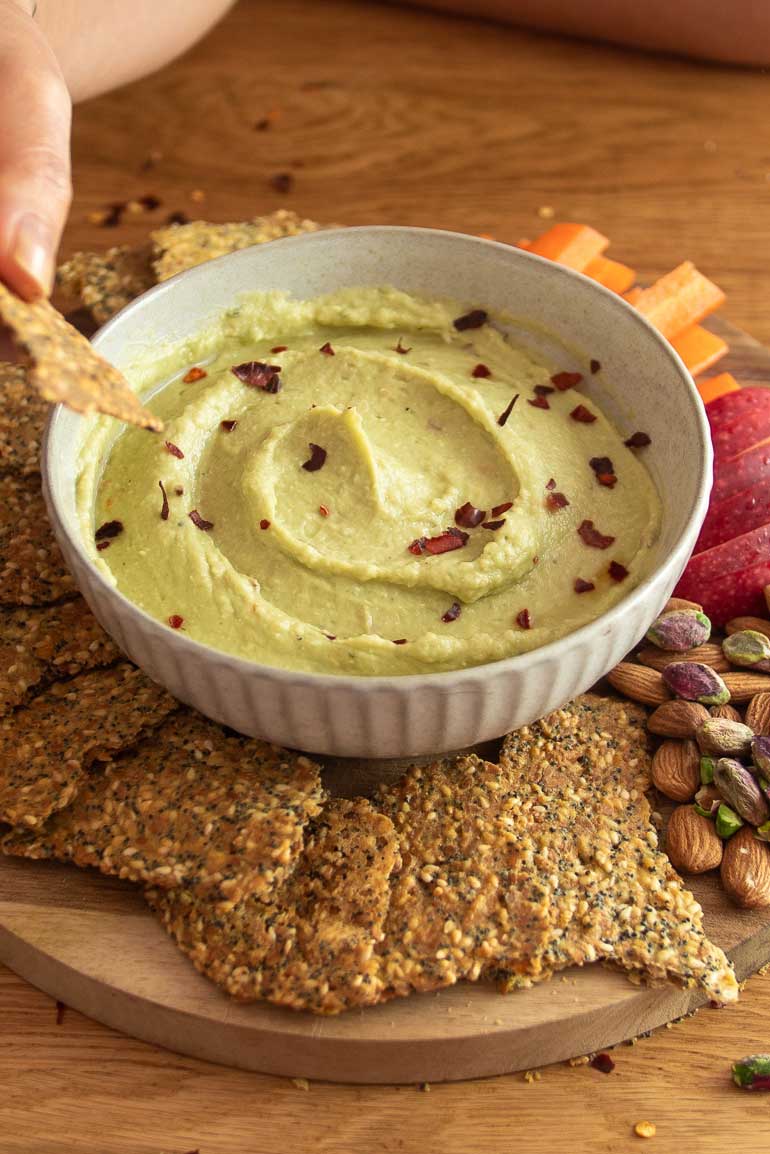 A bowl of creamy avocado bean dip surrounded by homemade nourishing crackers