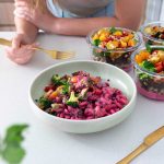 Vibrant pink bowl of Barbie Rainbow Veggie Pasta and meal prep containers