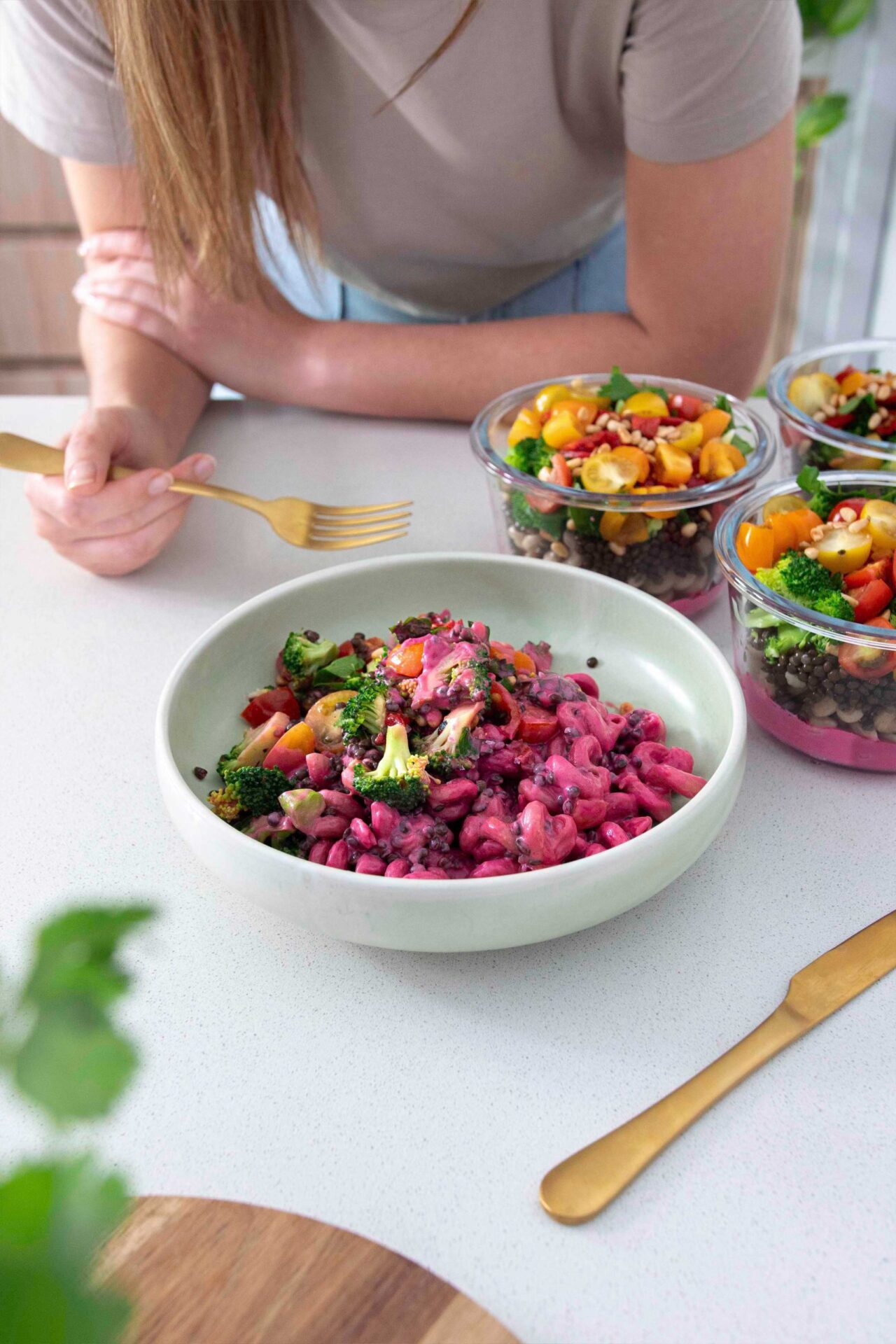 Vibrant pink bowl of Barbie Rainbow Veggie Pasta and meal prep containers