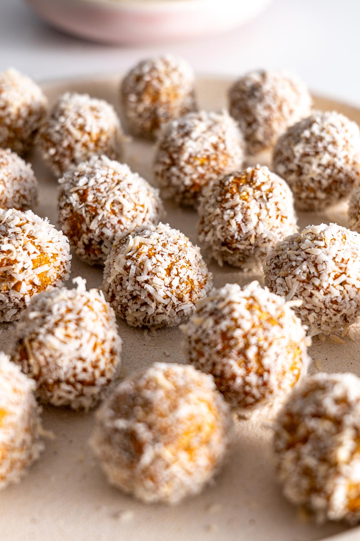A plate full of Carrot Cake Bliss Balls rolled in shredded coconut.