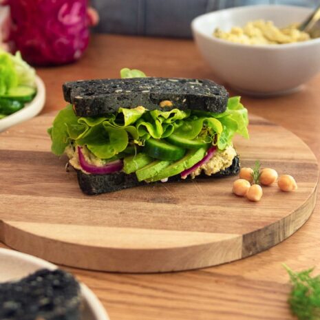 A mouthwatering chickpea-tuna sandwich with a creamy filling, topped with fresh lettuce and tomato slices, served on a toasted bun.