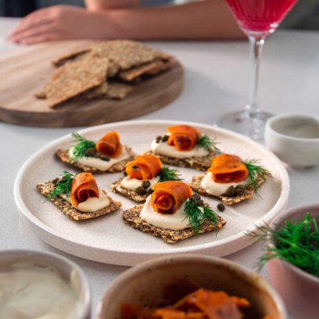 Vegan cream cheese carrot lox canapés arranged on a platter, topped with fresh dill and served with crackers.