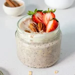 A festive overnight oats jar with gingerbread flavoured oats, topped with greek yogurt, cinnamon, pecans and strawberries