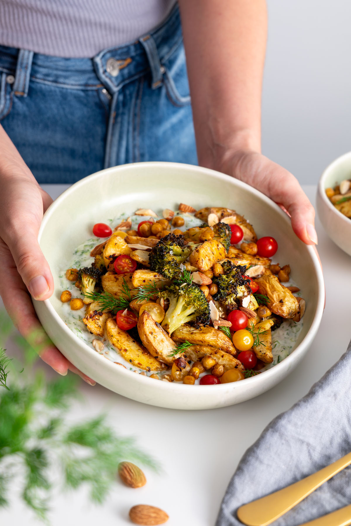 Hands placing a bowl of roasted potatoes, chickpeas, and broccoli on a table.
