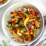A close-up of a bowl with roasted potatoes, broccoli, and chickpeas on a bed of tzatziki.
