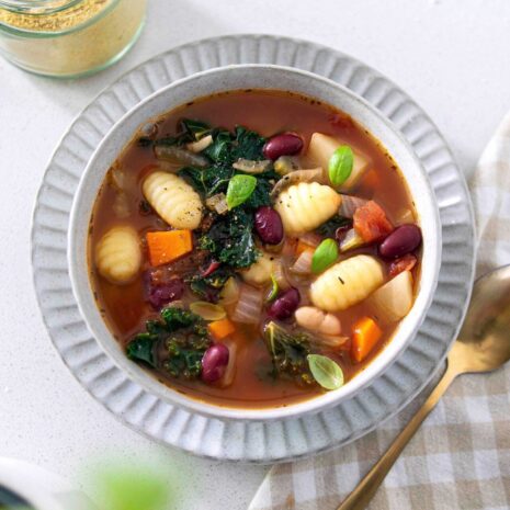 A bowl of hearty minestrone soup filled with vegetables, beans, and pasta, topped with a sprinkle of vegan cheese.