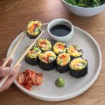 Plant-based rainbow sushi rolls on a plate with chopsticks