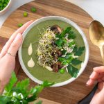 Vibrant green soup with sprouts and other herbs on a wooden serving board