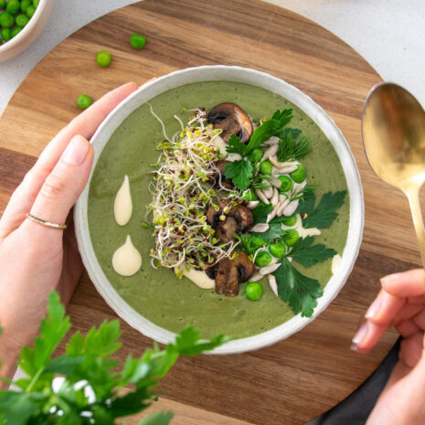 Vibrant green soup with sprouts and other herbs on a wooden serving board