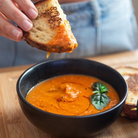 a vibrant bowl of roasted tomato soup with a cheesy sandwich being dipped