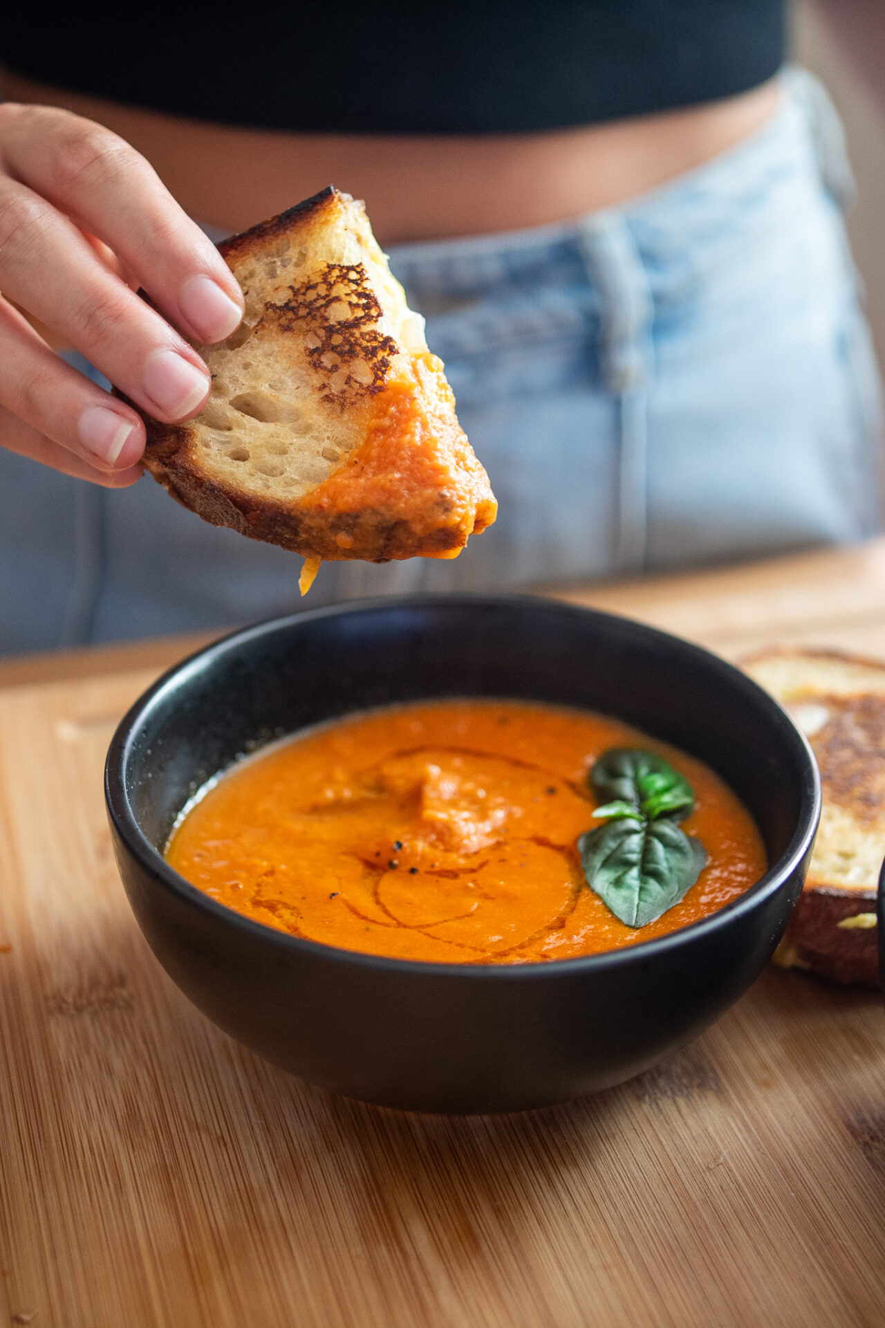 a vibrant bowl of roasted tomato soup with a cheesy sandwich being dipped