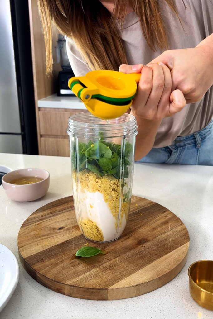 Blender jug with colorful ingredients inside while Sarah juices a lemon juice into it