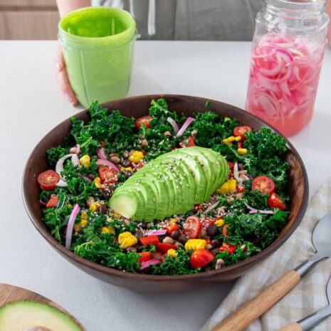 2-Bean avocado salad in a big wooden salad bowl with a jar of vibrant green dressing