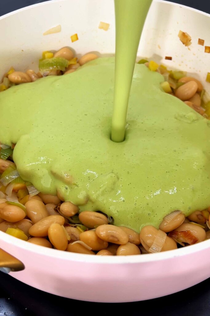 Pouring a vibrant green sauce on the butter beans in the pot