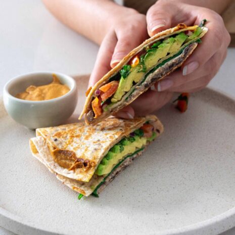 Sarah holding an avocado tortilla wrap over a dish with another wrap and ramekin with dipping sauce