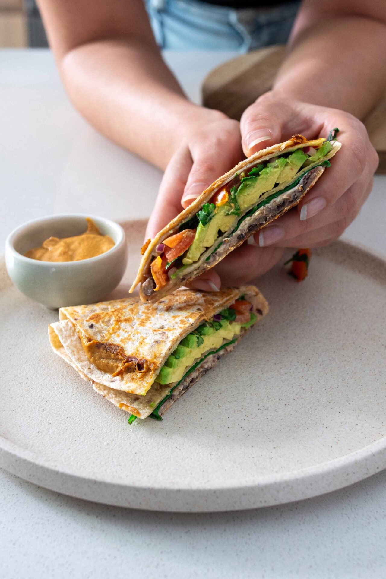 Sarah holding an avocado tortilla wrap over a dish with another wrap and ramekin with dipping sauce