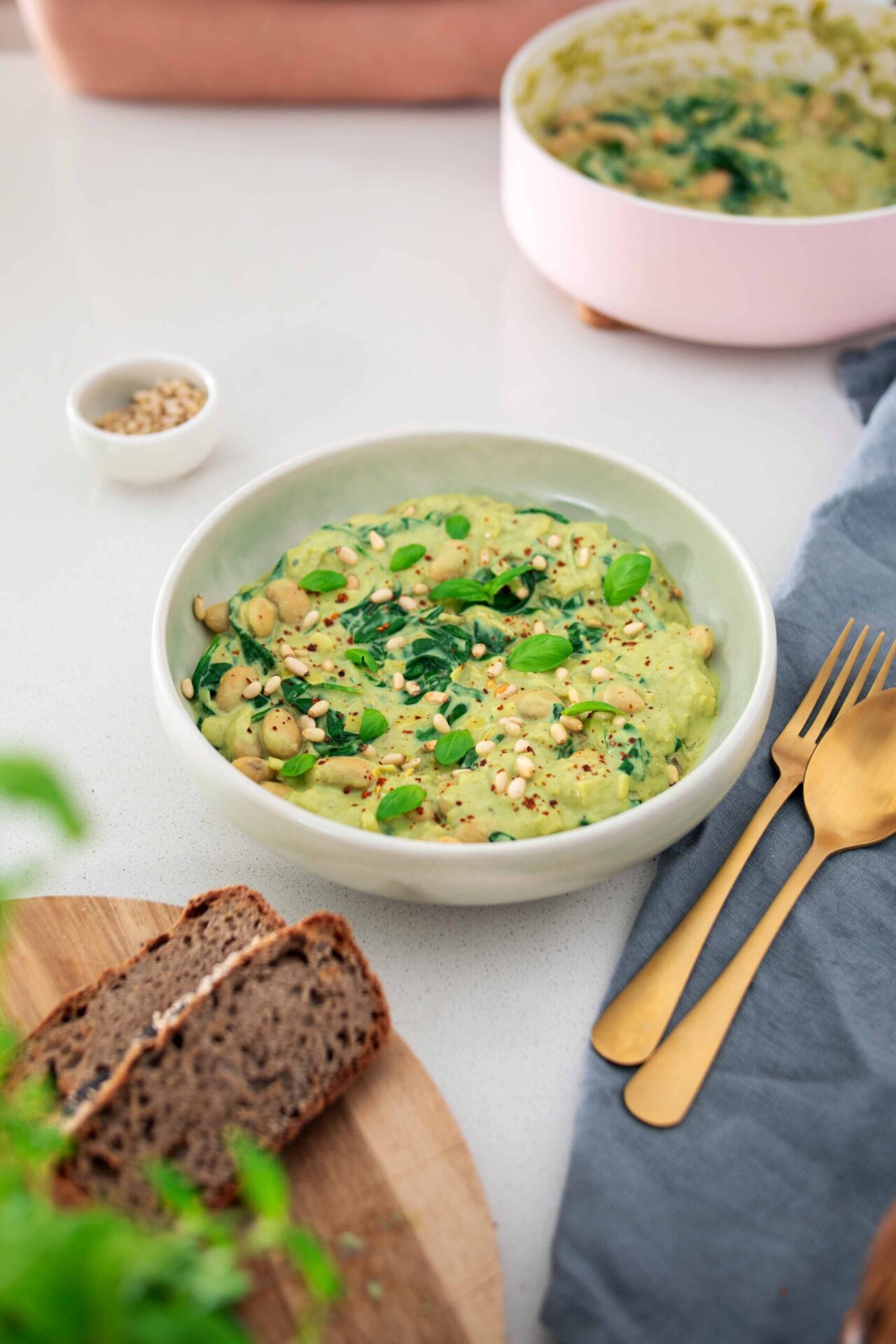A bowl of vibrant green butter bean pesto with buckwheat bread on the side