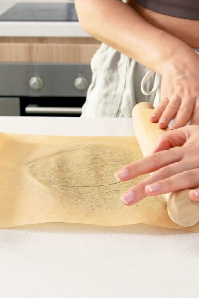 Crackers ingredients on baking paper being rolled flat