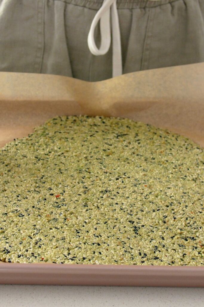 The flattened cracker mix on a piece of baking paper, inside of an oven tray