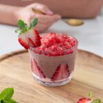 A colorful chocolate and strawberry chia pudding with shaved frozen strawberry ice on top. Served on a wooden board.