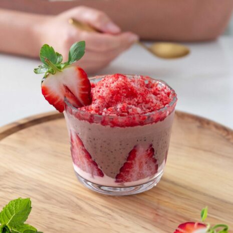 A colorful chocolate and strawberry chia pudding with shaved frozen strawberry ice on top. Served on a wooden board.