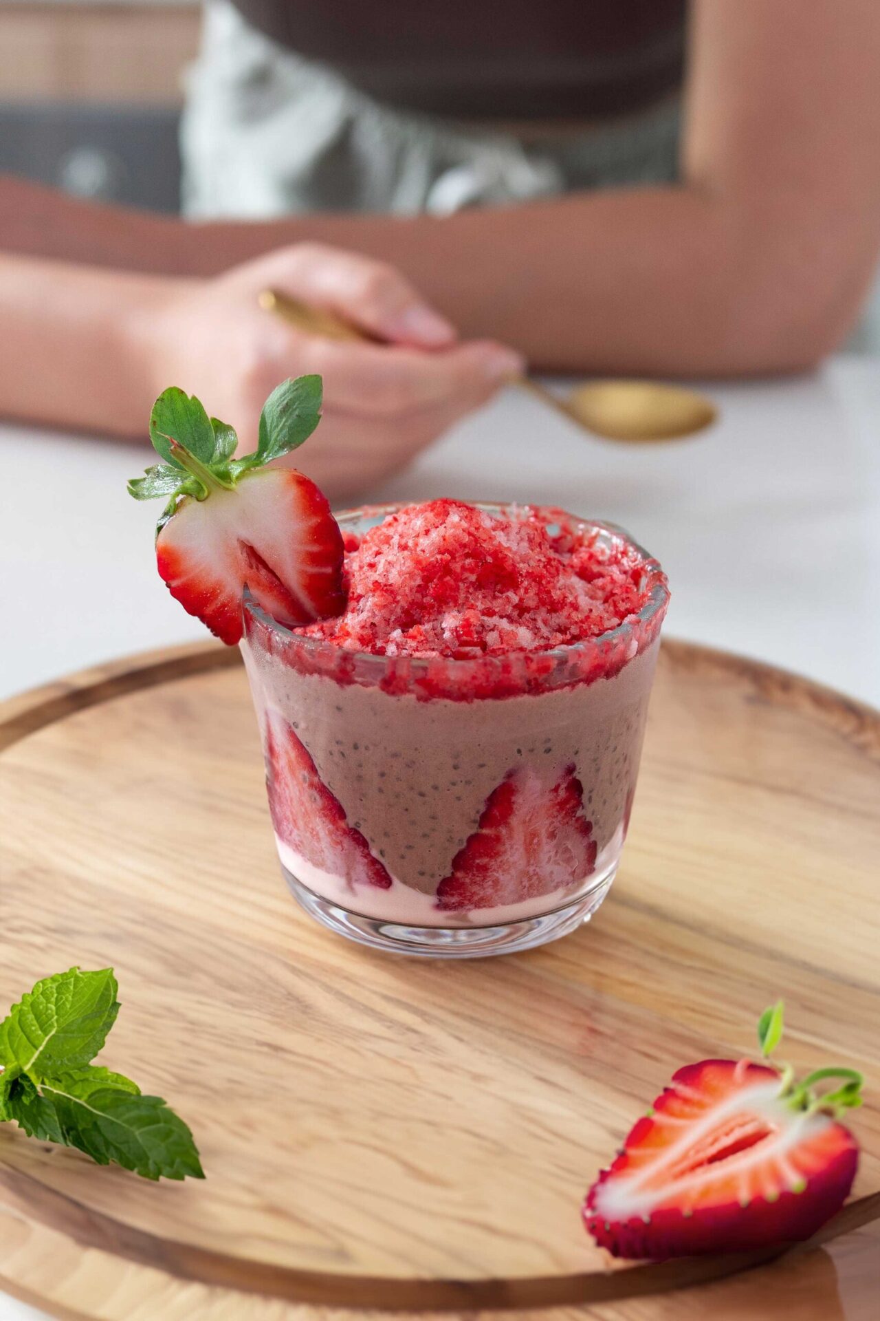 A colorful chocolate and strawberry chia pudding with shaved frozen strawberry ice on top. Served on a wooden board.