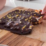 Slab of dark chocolate date park topped with pistachios on a wooden chopping board
