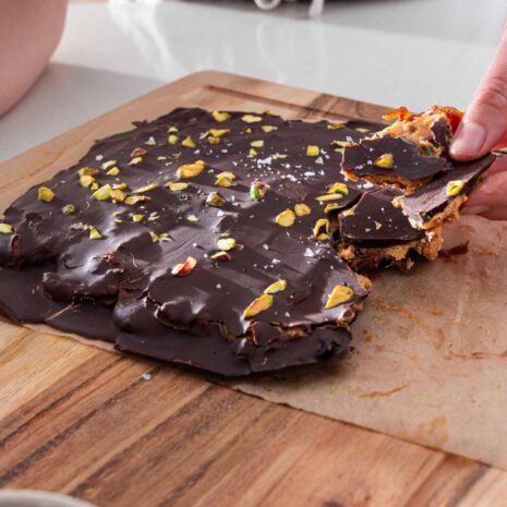 Slab of dark chocolate date park topped with pistachios on a wooden chopping board