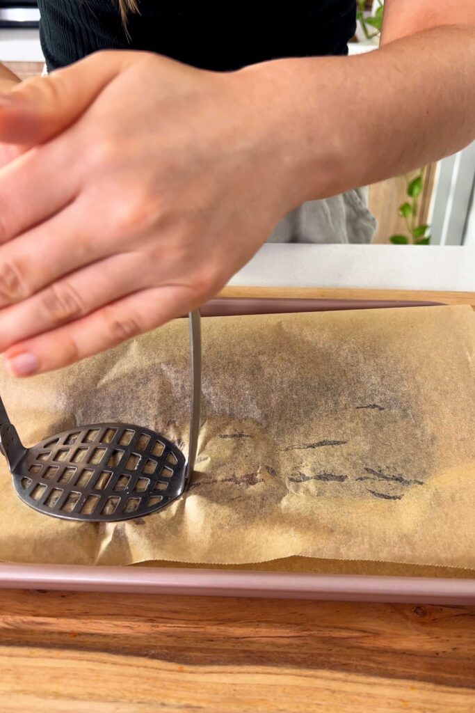 Mashing the dates between baking paper with a potato masher