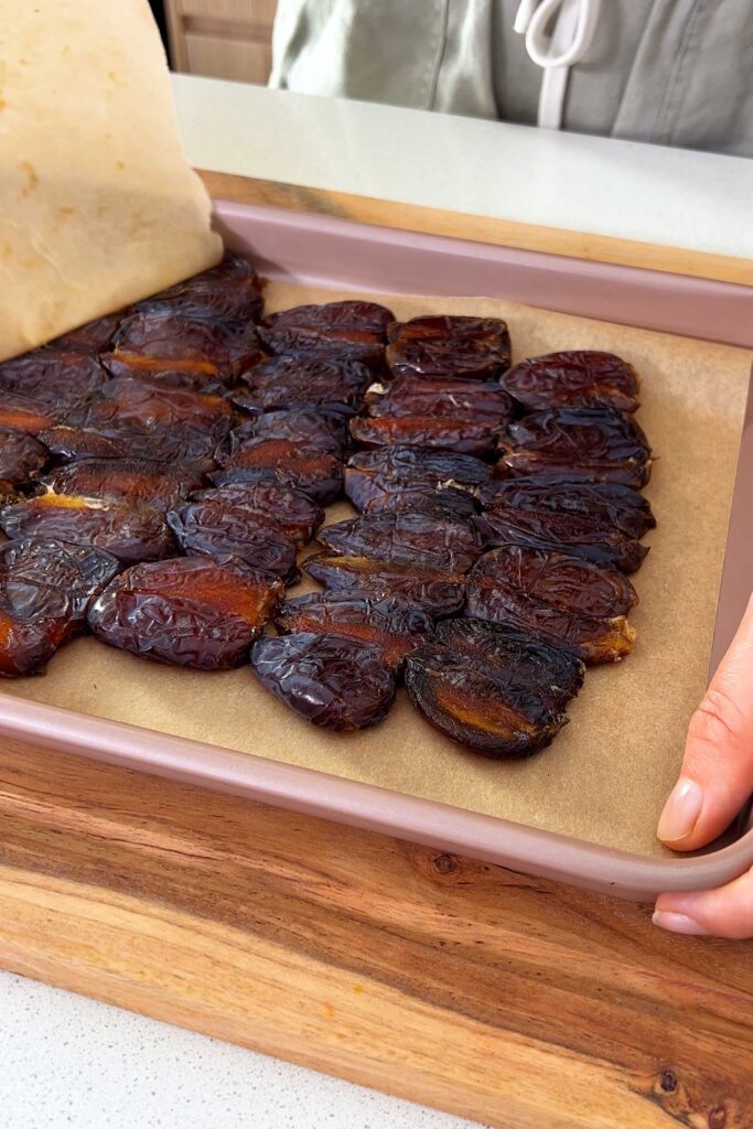 Lifting the baking paper to reveal the flattened Medjool dates