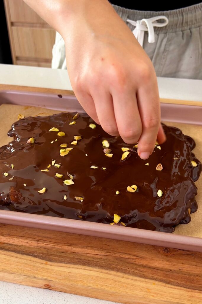 Topping the Medjool date bark, peanut butter and melted chocolate with chopped pistachios