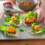 Crispy cauliflower wings on a bed of beetroot hummus, lettuce leaves on a serving platter