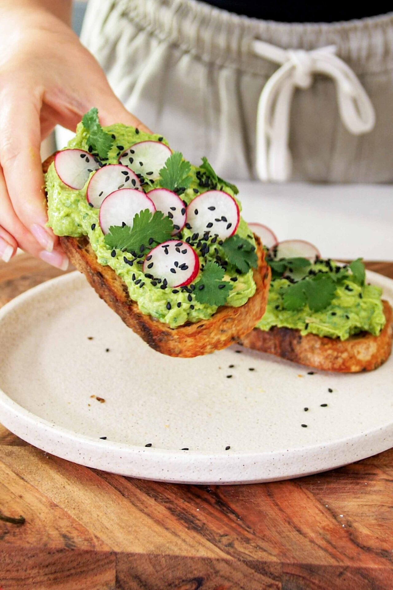 Sarah holding a Smashed peas and avocado toast on a white plate on a wooden serving board