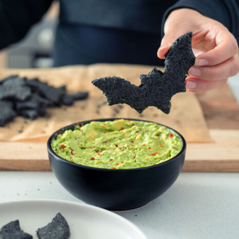 Black bat shaped cracker hovering over a bowl of guacamole