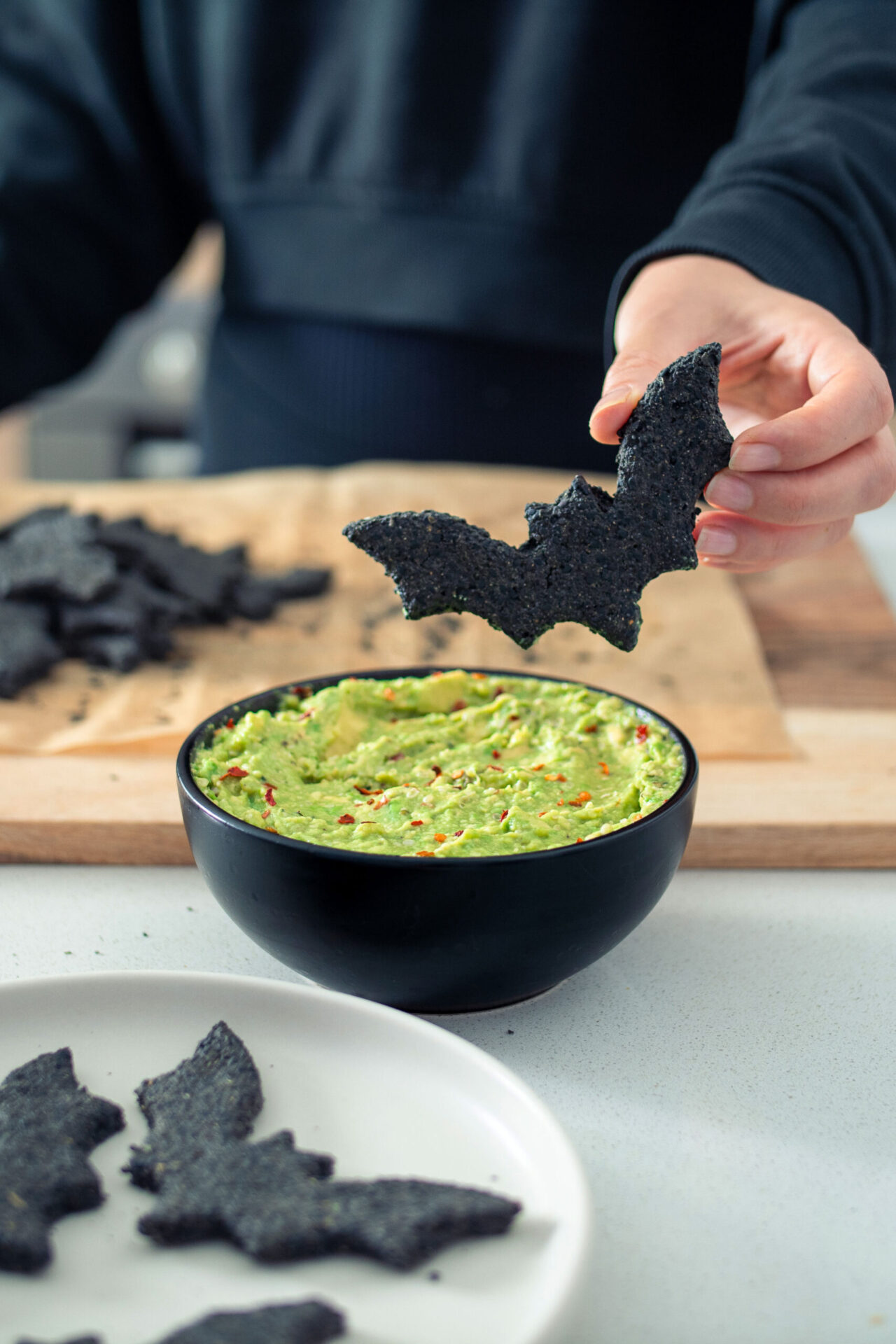 Black bat shaped cracker hovering over a bowl of guacamole