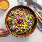 Full view of mixed High Protein Soba Noodle Salad with Peanut Sauce in a wooden bowl with serving spoons on the side.