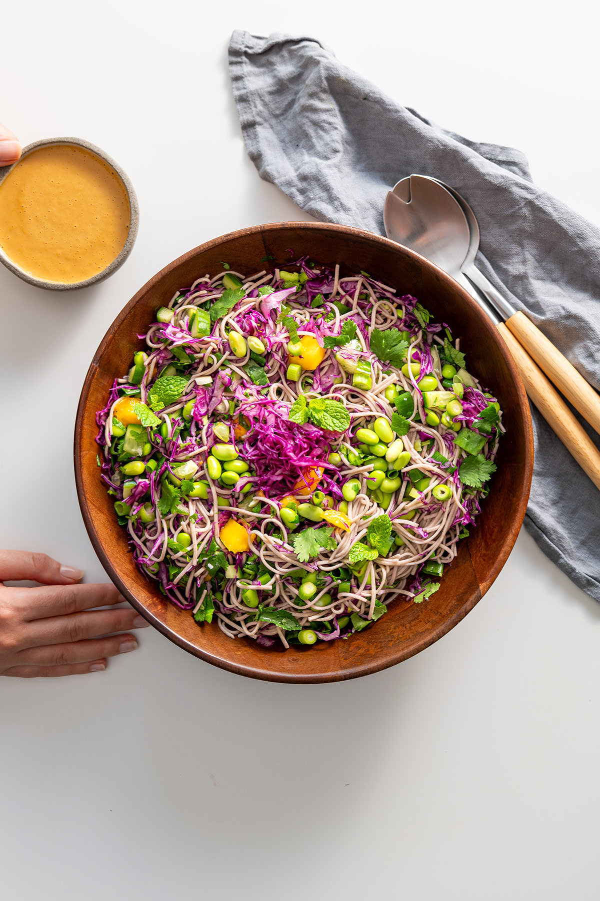 Full view of mixed High Protein Soba Noodle Salad with Peanut Sauce in a wooden bowl with serving spoons on the side.