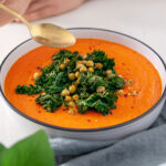 Big bowl of bright orange Roasted Cauliflower and Red Pepper Soup covered in green roasted Kale and Chickpeas