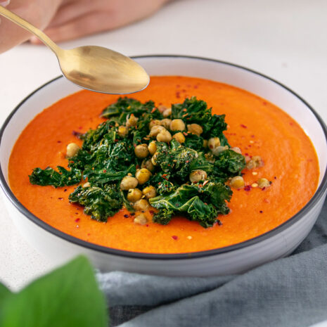 Big bowl of bright orange Roasted Cauliflower and Red Pepper Soup covered in green roasted Kale and Chickpeas