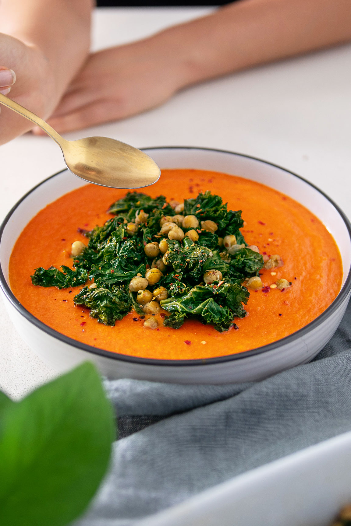 Big bowl of bright orange Roasted Cauliflower and Red Pepper Soup covered in green roasted Kale and Chickpeas