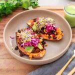A bowl with vibrant, colorful roasted sweet potatoes topped with beans, veggies, cabbage slaw and sprouts