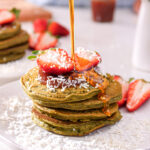 Maple syrup pouring over a vibrant green stack of Matcha Avocado Gluten-Free Christmas Pancakes
