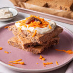 Stack of square sheet pan Carrot Cake Pancakes with yogurt icing and shredded carrot