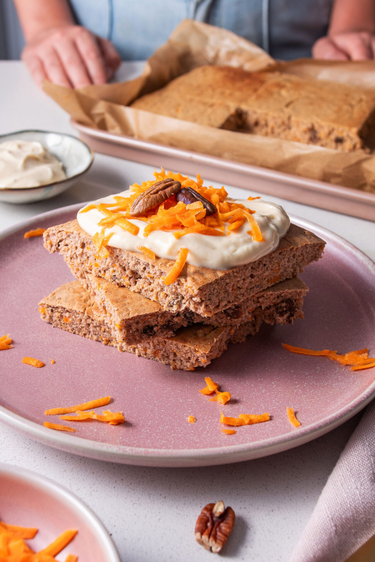 Stack of square sheet pan Carrot Cake Pancakes with yogurt icing and shredded carrot