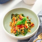 Plate of Mediterranean orzo salad with fresh spinach, tomatoes, and pine nuts, served with a gold fork and gray napkin.