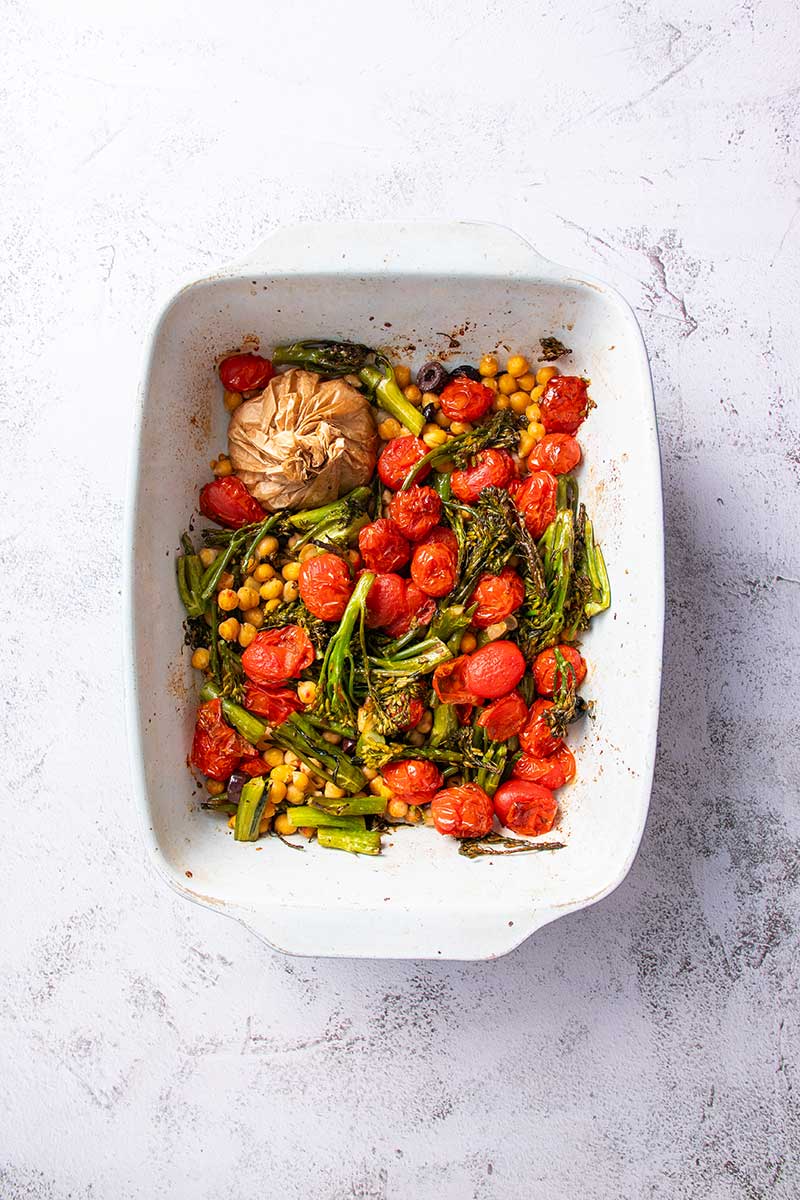 Golden-brown roasted chickpeas with cherry tomatoes and asparagus in a white baking dish.
