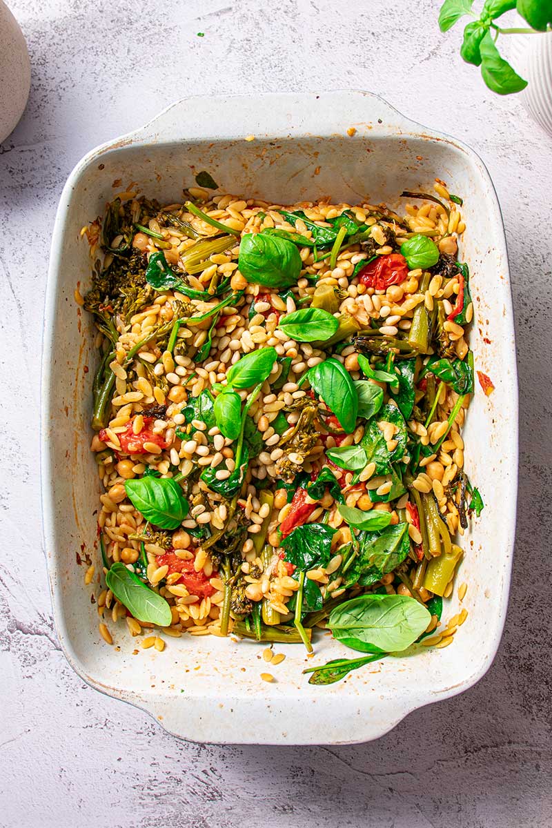 Overhead view of orzo combined with roasted green vegetables and tomatoes, sprinkled with fresh basil.